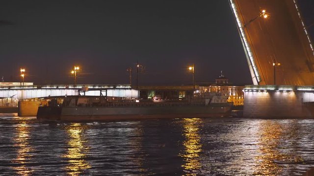 Night. Barge, cargo ship floats through a drawbridge along the Neva River in Saint Petersburg.
