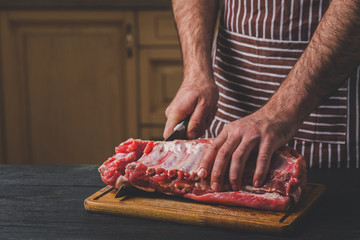 Man cuts of fresh piece of meat on a wooden cutting board in the home kitchen