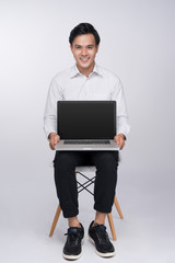 Smart casual asian man seated on chair, showing laptop screen in studio background