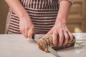 Woman cutting bread on wooden board. Bakehouse. Bread production.