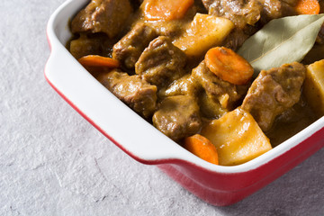 Beef meat stewed with potatoes, carrots and spices in ceramic pot on gray stone
