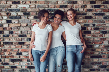 Three attractive girls in white T-shirts are standing on a brick wall background.