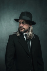 Retro victorian style man with blond long hair and hat. Wearing black suit and tie.