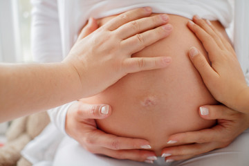 Several hands touch the belly of a pregnant woman. She hugs her stomach with well-groomed hands with a neat French manicure