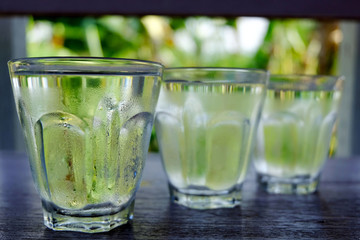Row of water glass on wooden table on bright green background