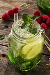 Tasty cold fresh drink lemonade with lemon, mint, ice, raspberry and lime in glass on wooden table. Closeup.