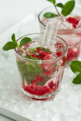 Tasty cold fresh drink lemonade with raspberry, mint, ice and lime in glass on white plate with ice background. Closeup.