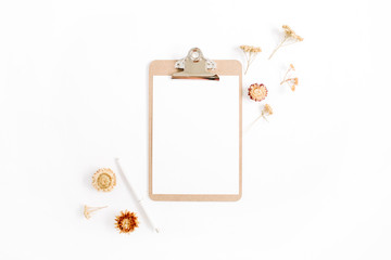 Clipboard mock up and pale dried flowers on white background. Flat lay, top view minimalistic brown styled home office desk. Beauty blog concept.