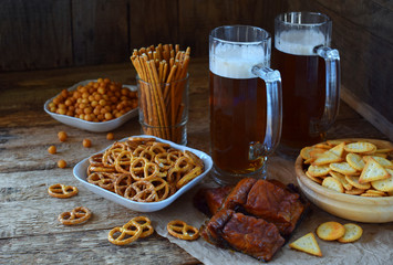 Football fan set with mugs of beer and salty snacks on wooden background. Crackers, pretzel, salted straws, nuts, dried fish. Junk food for beer or cola. Photographed with natural light