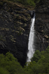 Water dripping down a tall mountain waterfall with lush vegetation,rocks and grass