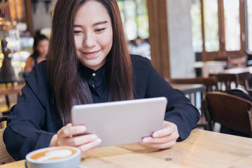 A beautiful Asian woman with smiley face using tablet in modern cafe