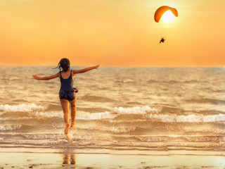 The girl runs into the sea pretending to parody the paramotor flying in the evening, the sun is falling, the concept of relaxation.
