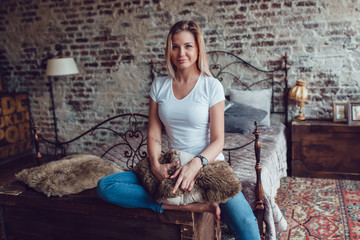 Attractive blonde woman is sitting at home near the bed.