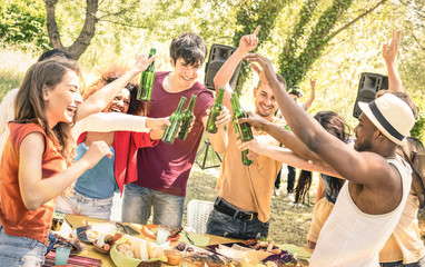 Young multiracial friends toasting beer at barbecue garden party - Friendship concept with happy people having fun at backyard summer camp - Food and drinks fancy dinner with dj music set outdoors