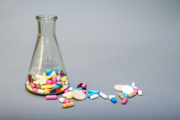 Colorful medical pills in a glass container on a grey background.