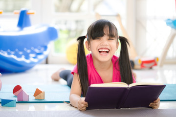 Cute little girl is reading a book . Funny kid having fun in kids room