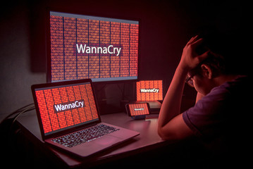 Young Asian male frustrated, confused and headache by WannaCry ransomware attack on desktop screen,...