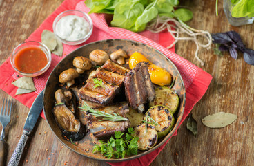 Grilled ribs with mushrooms and zucchini in a frying pan on a table