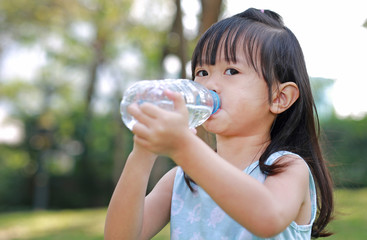 Close Up little girl drinking water from bottle in the park. Portrait outdoor.