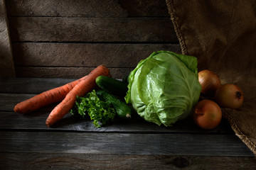 still life with vegetables. cabbage, carrots, onions, cucumbers, parsley on wooden background with beautiful sun