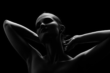Black and white shot of woman posing sensually holding head up on black background, monochrome