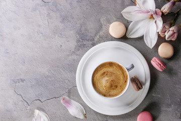 White cup of black coffee, served on white saucer with macaroons biscuits and magnolia flower...