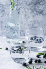 Tonic water cocktail with rosemary and blueberries. Two cold glasses and bottle with bubbles over gray blue texture background. Refreshing beverage alco non alcohol