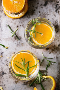 Tonic water cocktail with rosemary and orange. Two glasses with zest sugar and bubbles with textile over dark texture metal background. Refreshing beverage alco non alcohol. Top view