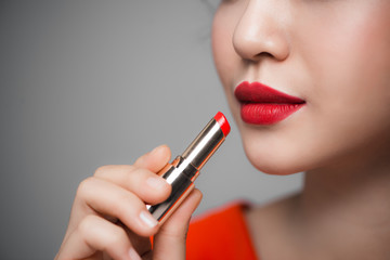 Close up portrait of attractive girl holding red lipstick over grey background