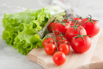 Ripe tomatoes and green salad on the kitchen table, cutting board.Morning light.