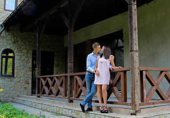 Obraz na płótnie Canvas Couple hugs and kissing near house veranda. Girl dressed in pink dress and man in blue shirt and jeans.