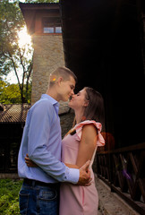 Couple hugs and kissing near house. The warm light of the sun. Girl dressed in pink dress and man in blue shirt and jeans.