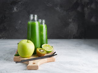 Fresh green smoothies from the green fruits and vegetables on a wooden Board.Concrete grey background.Glass bottle.