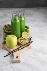 Fresh green smoothies from the green fruits and vegetables on a wooden Board.Concrete grey background.Glass bottle.