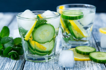 Lemon and cucumber detox water on blue colored wooden background.
