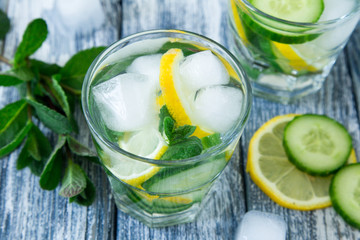 Lemon and cucumber detox water on blue colored wooden background.