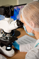 Laboratory assistant or technician in medical research lab looking into a microscope and doing research