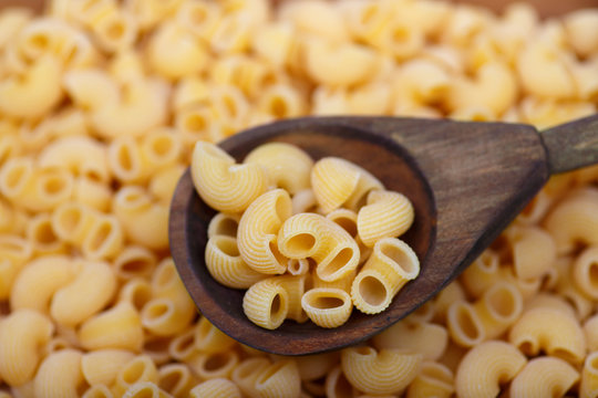 A wooden spoon with chifferi pasta in the foreground. Background with paste blurred