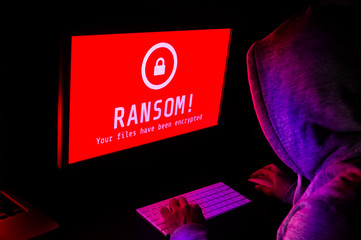 Computer screen with ransomware attack alerts in red and a hacker man keying on keyboard in a dark room, ideal for online security failure and digital crime