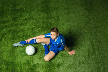 Fototapeta na wymiar Boy soccer player sitting on green grass