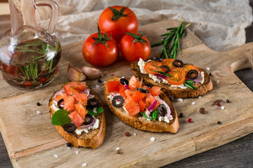 Brushetta set. Variety of small sandwiches with prosciutto, tomatoes, parmesan cheese,    Black olives, fresh basil on rustic wooden board over dark background