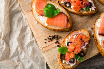 Italian bruschetta set. Varied sandwiches with cheese and red fish, roasted tomatoes, fresh basil, spices, rosemary, garlic, onion, chili pepper.  on rustic wooden board over dark background, top view