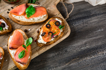 Italian bruschetta set. Varied sandwiches with cheese and red fish, roasted tomatoes, fresh basil, spices, rosemary, garlic, onion, chili pepper.  on rustic wooden board over dark background, top view