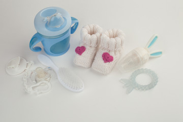 Baby accessories background: booties, tiny rod, soother, brush, and toys over white background with copy space; top view. Concept of Infancy and motherhood