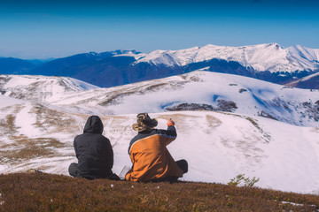 Fototapeta premium Two hikers sit on a hill and enjoy the mountain valley