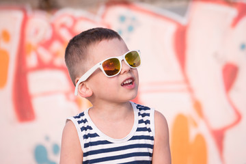 Adorable small boy wearing sunglasses and singlet on graffiti wall backgound