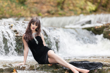 Young girl in a black dress posing on the edge of a waterfall