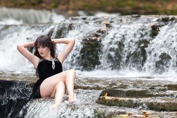 Young girl in a black dress posing on the edge of a waterfall