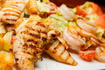 Close-up of salad of romaine lettuce with prawns, smocked salmon, croutons, grilled chicken, cherry tomatoes with caesar dressing and grated parmesan