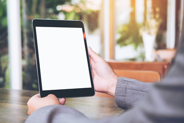 Mock up image of business woman's hands holding black tablet with white blank screen in cafe with nature background